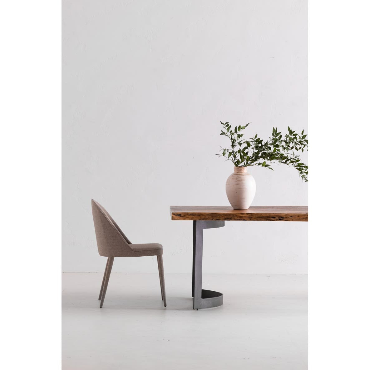 Minimalist interior with a wooden table and chair against a white wall.