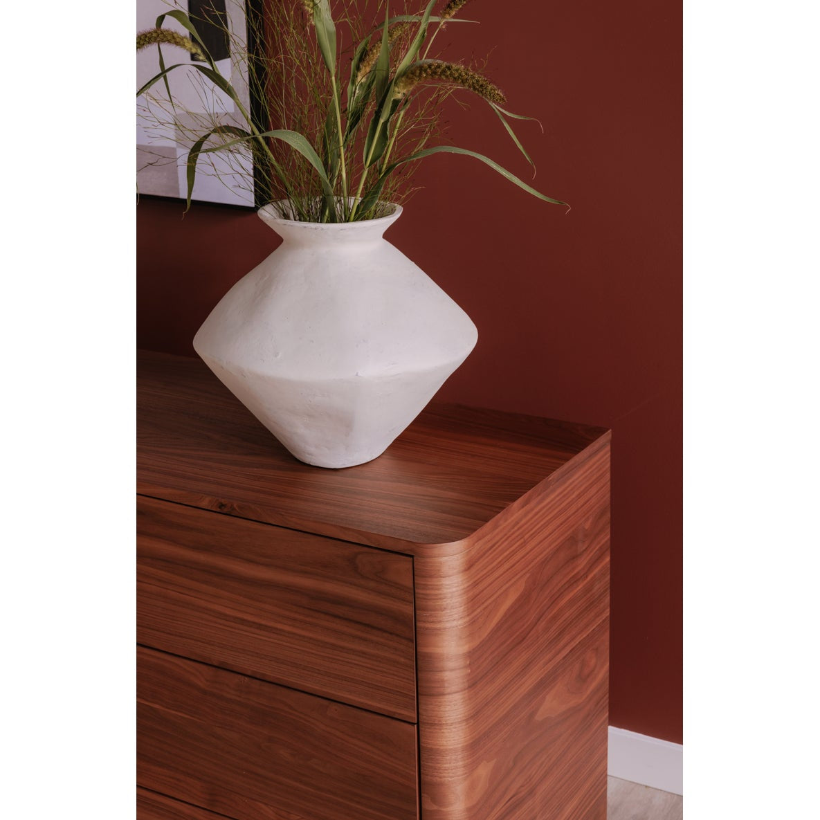 Wooden dresser with a white vase and plant against a red wall