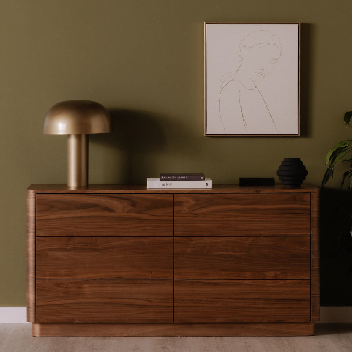 Wooden dresser against a green wall with decorative items and a plant.