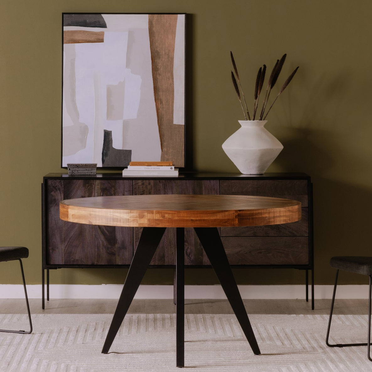 Modern dining set with round wooden table and two chairs against a green wall.