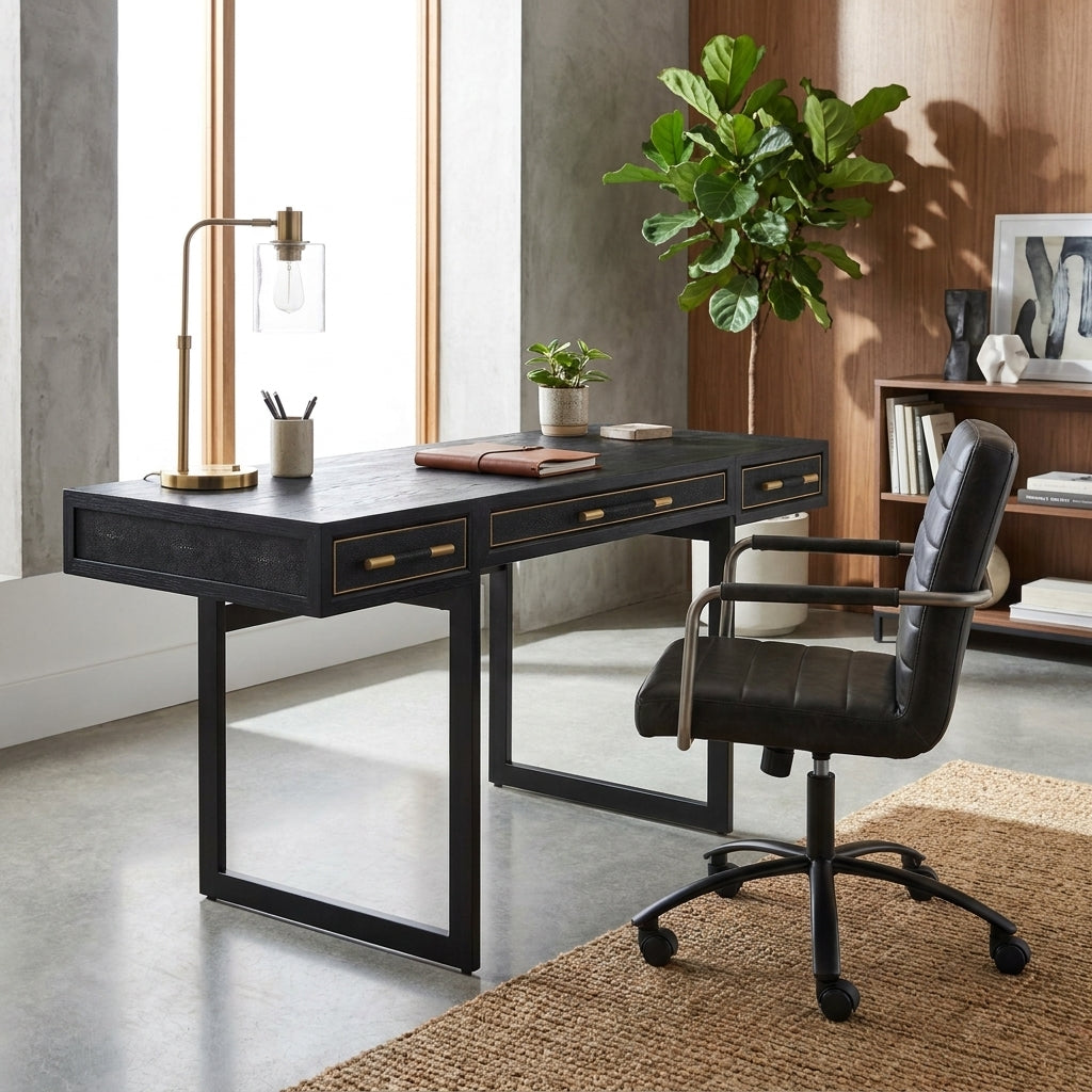 A black writing desk with gold drawer pulls and a matching black office chair in a modern home office setting with a plant, lamp, and shelving.