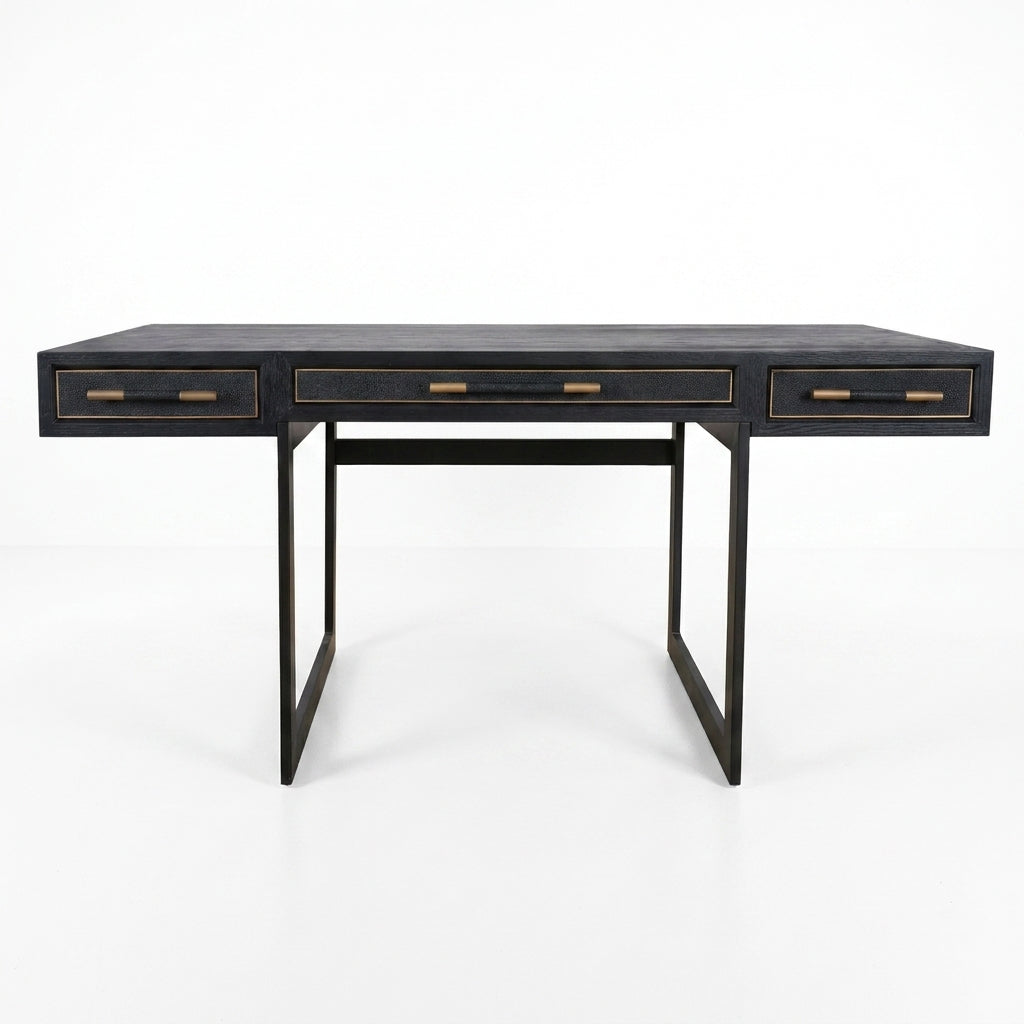 A black writing desk with three drawers, featuring gold-toned metal handles and trim, supported by a minimalist black metal frame on a white background.