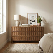 A light natural wood six-drawer dresser in a styled bedroom setting, decorated with a vase of green leaves, a framed print, books, and a bowl.