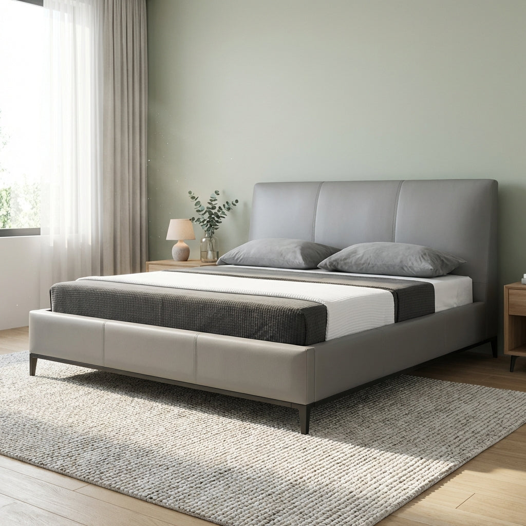 Gray upholstered bed in a room with light green walls and wooden flooring.