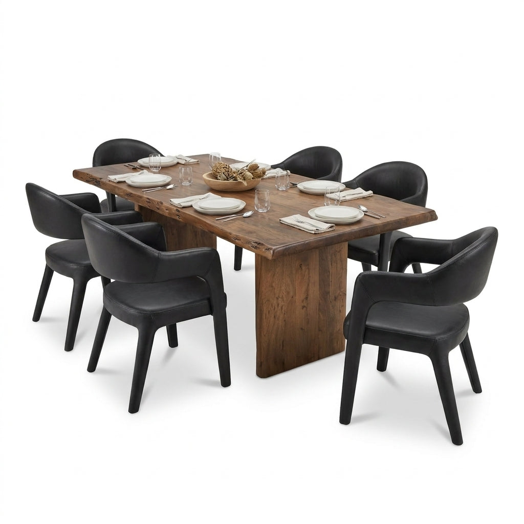 A modern dining set featuring a rectangular wooden table with a rustic live-edge top and a matching dark wood pedestal base, surrounded by six black upholstered dining chairs. The table is styled with white plates, folded napkins, and a small woven centerpiece bowl, set against a plain white background.