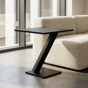 Modern black side table in a living room setting with a beige sofa and large windows.