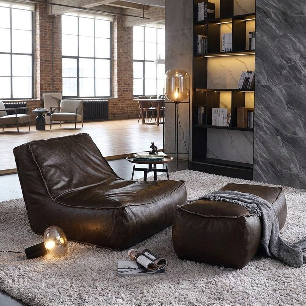 Brown leather bean bag chair and ottoman in a modern living room with large windows and bookshelves.