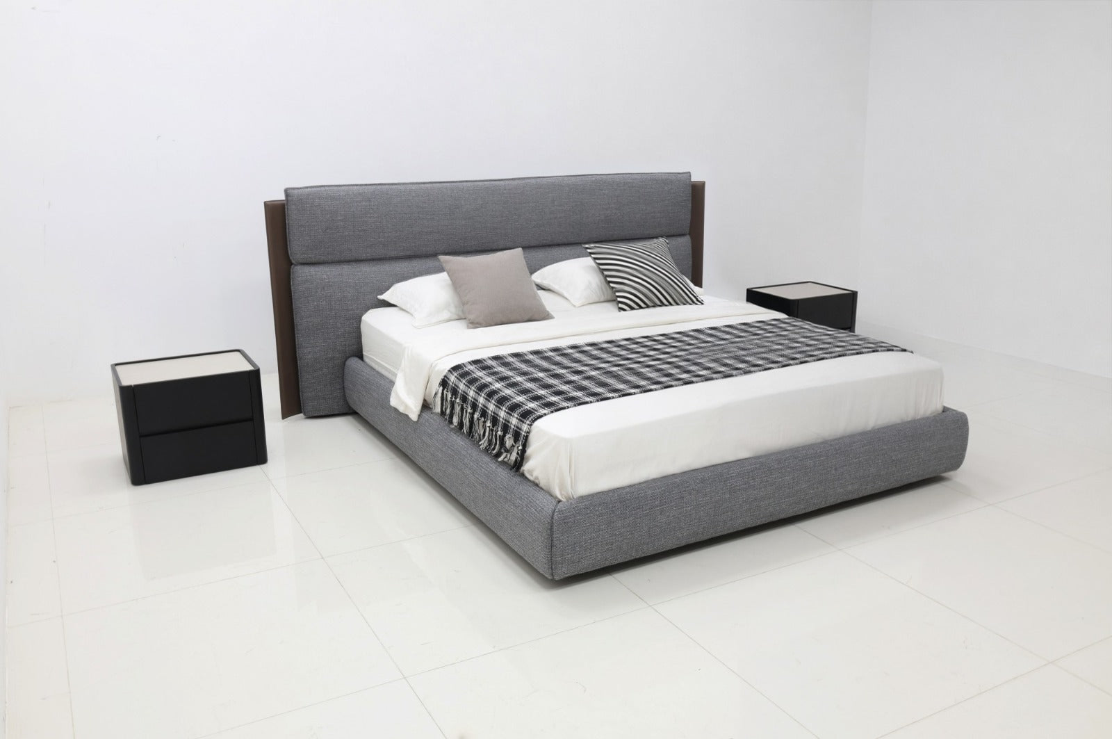 A modern platform bed with a gray upholstered frame and headboard, styled with white bedding, a black-and-white checkered throw blanket, and accent pillows. It is flanked by two black nightstands in a bright, minimalist white bedroom.