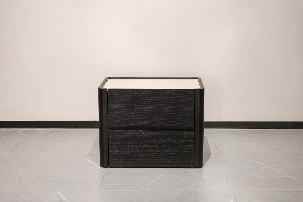 A modern two-drawer nightstand or storage cabinet with a dark textured wood finish and a light top surface, shown in a minimalist room setting with a light gray tiled floor and off-white wall.