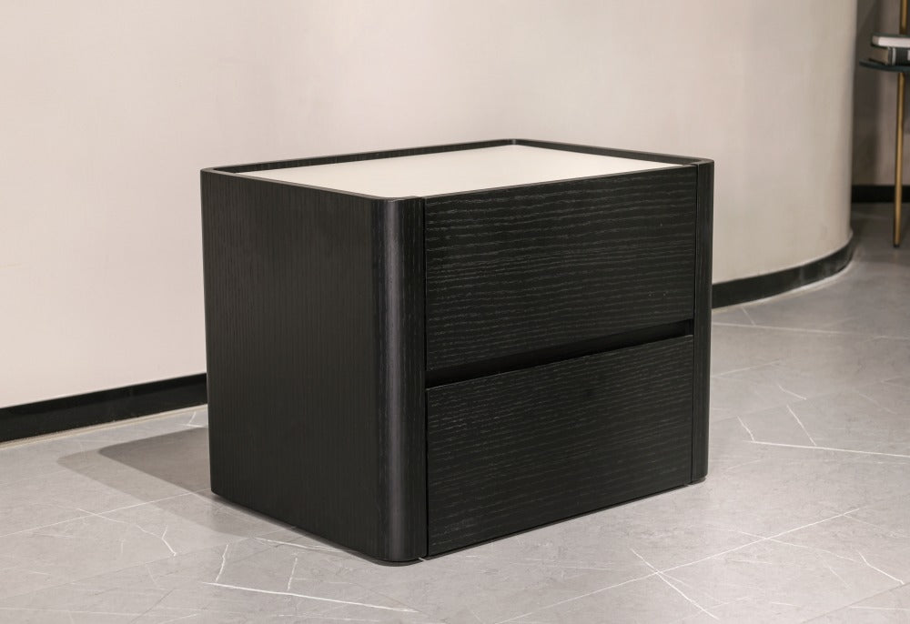 A modern black two-drawer nightstand or side table with a white top surface, shown in a minimalist interior setting with gray tiled flooring and a light beige wall.