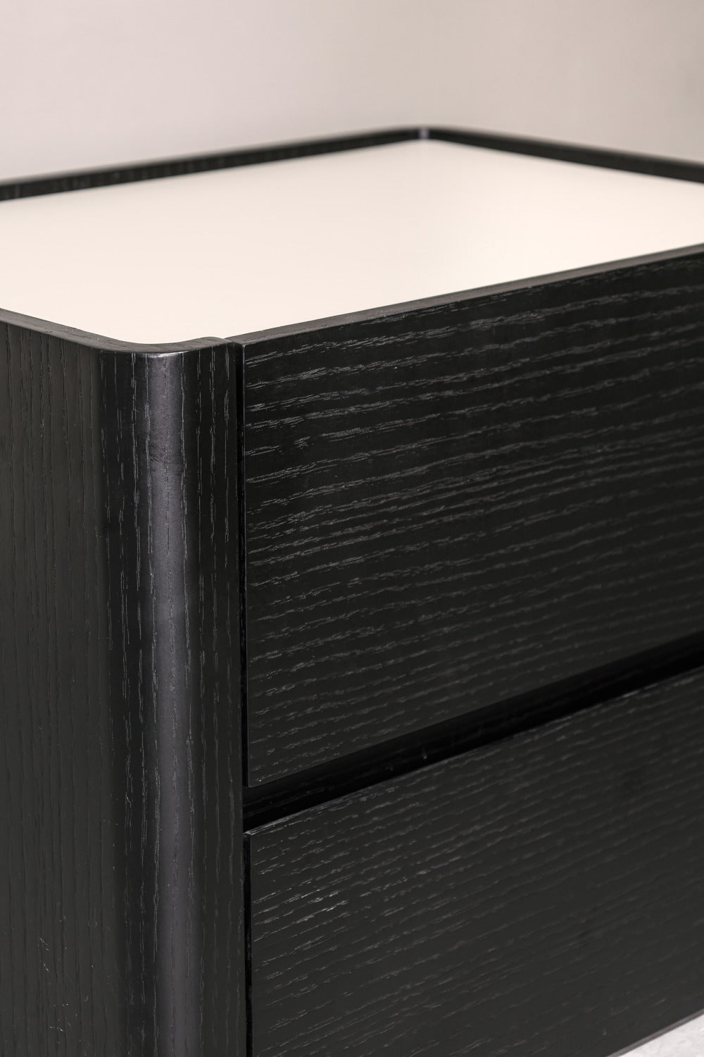 Close-up of a black wood-grain drawer unit with a white top surface, showing the drawer front and part of the top edge.