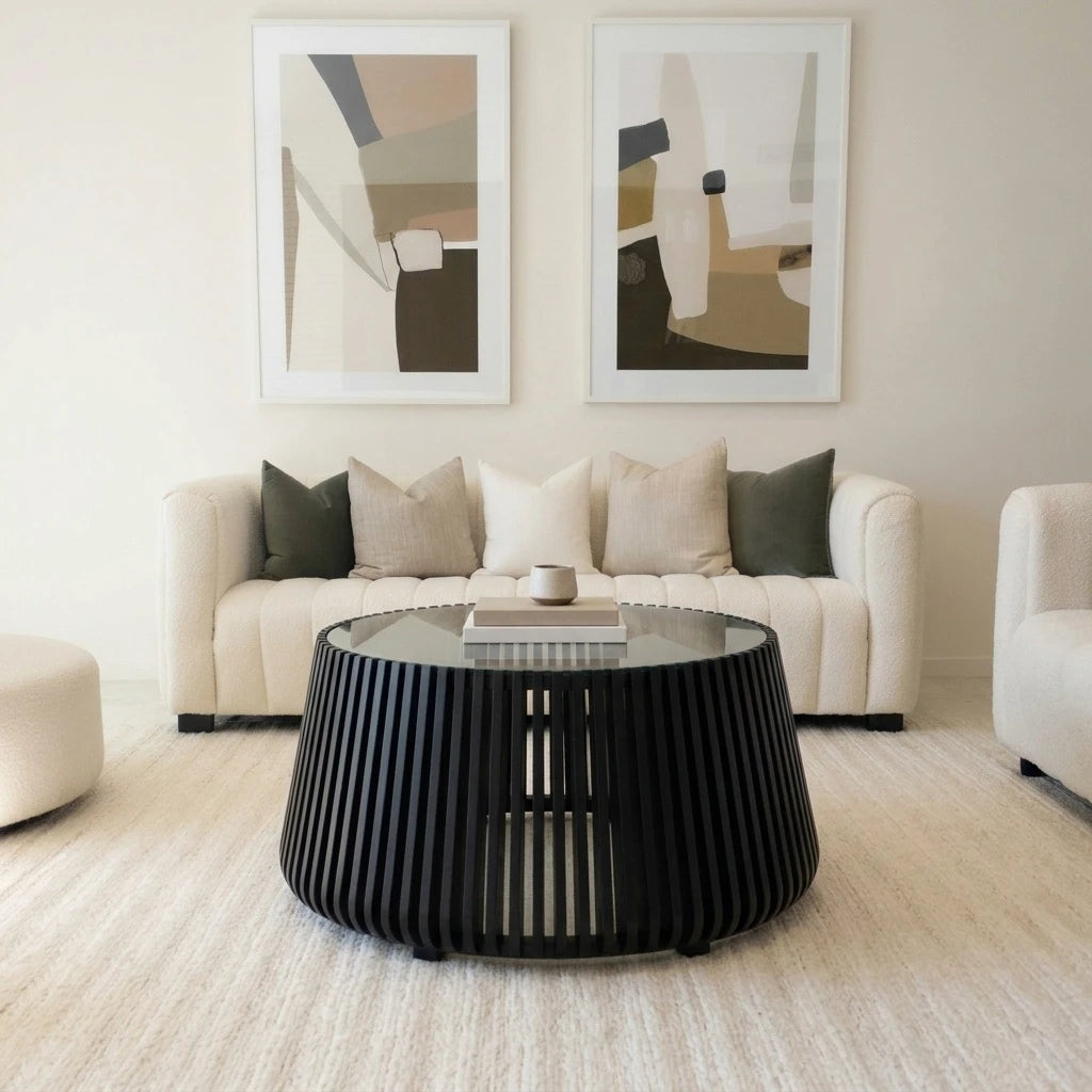 Barga round black acacia coffee table with glass top in front of a cream sofa