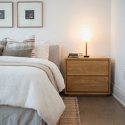 Timberton Nightstand in White Oak beside a bed
